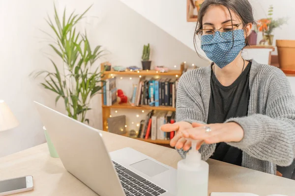 Coronavirus. Young business woman isolated working from home wearing home made protective mask. Woman in quarantine for coronavirus using sanitizer gel meanwhile she is working. Quarantine.