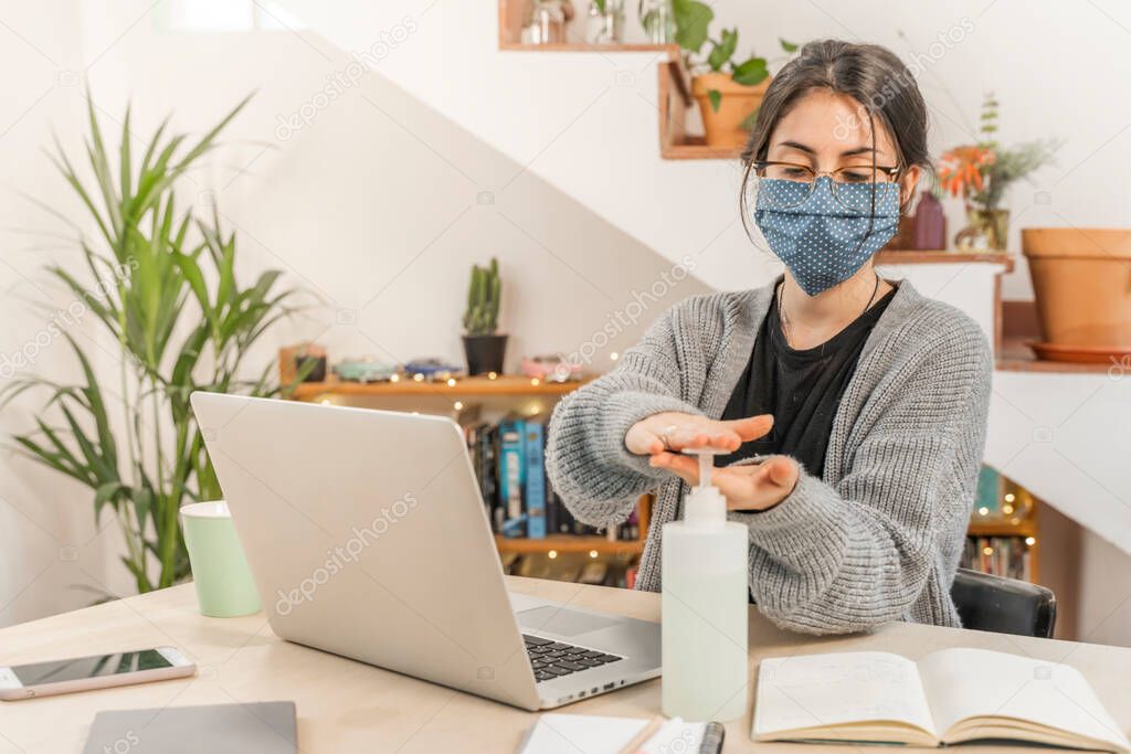 Coronavirus. Young business woman isolated working from home wearing home made protective mask. Woman in quarantine for coronavirus using sanitizer gel meanwhile she is working. Quarantine. 