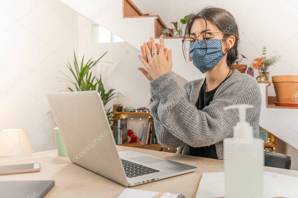 Coronavirus. Young business woman isolated working from home wearing home made protective mask. Woman in quarantine for coronavirus using sanitizer gel meanwhile she is working. Quarantine. 