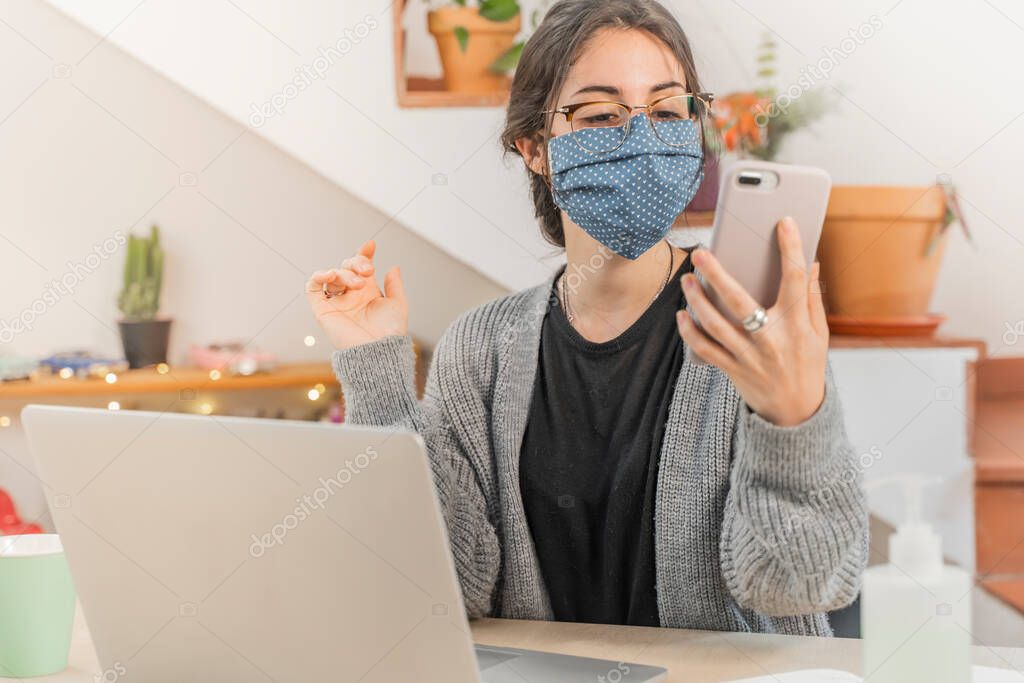 Coronavirus. Young business woman isolated working from home wearing protective mask. Woman in quarantine for coronavirus wearing home made mask. Working with mobile phone. Quarantine. 