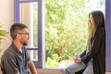 Coronavirus. Arkadaşları evde kahve yapıyor ve Coronavirus sırasında pencerenin yanında konuşuyorlar. Karantina konsepti. İşçiler. İzole edilmiş. Mola zamanı..