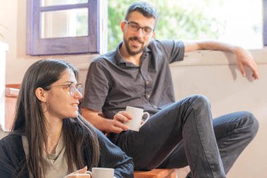 Coronavirus. Arkadaşları evde kahve yapıyor ve Coronavirus sırasında pencerenin yanında konuşuyorlar. Karantina konsepti. İşçiler. İzole edilmiş. Mola zamanı..