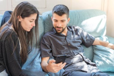 Coronavirus. Bir çift, Coronavirus sırasında evdeki karantinada kanepede oturuyor. Evdeki çift kanepede oturuyor, cep telefonuna bakıyor ve konuşuyor. - Eve. Evde kal.. 