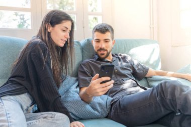 Coronavirus. Bir çift, Coronavirus sırasında evdeki karantinada kanepede oturuyor. Evdeki çift kanepede oturuyor, cep telefonuna bakıyor ve konuşuyor. - Eve. Evde kal.. 