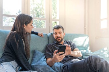 Coronavirus. Bir çift, Coronavirus sırasında evdeki karantinada kanepede oturuyor. Evdeki çift kanepede oturuyor, cep telefonuna bakıyor ve konuşuyor. - Eve. Evde kal.. 