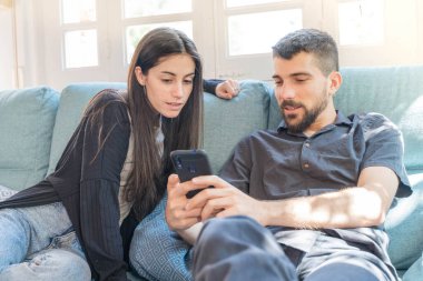 Coronavirus. Bir çift, Coronavirus sırasında evdeki karantinada kanepede oturuyor. Evdeki çift kanepede oturuyor, cep telefonuna bakıyor ve konuşuyor. - Eve. Evde kal.. 