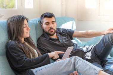 Coronavirus. Bir çift, Coronavirus sırasında evdeki karantinada kanepede oturuyor. Evdeki çift kanepede kitap izliyor ve konuşuyor. - Eve. Evde kal.. 