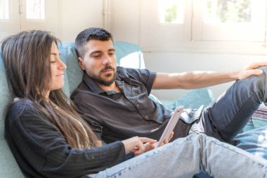 Coronavirus. Bir çift, Coronavirus sırasında evdeki karantinada kanepede oturuyor. Evdeki çift kanepede kitap izliyor ve konuşuyor. - Eve. Evde kal.. 