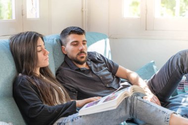 Coronavirus. Bir çift, Coronavirus sırasında evdeki karantinada kanepede oturuyor. Evdeki çift kanepede kitap izliyor ve konuşuyor. - Eve. Evde kal.. 