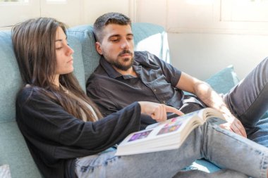 Coronavirus. Bir çift, Coronavirus sırasında evdeki karantinada kanepede oturuyor. Evdeki çift kanepede kitap izliyor ve konuşuyor. - Eve. Evde kal.. 