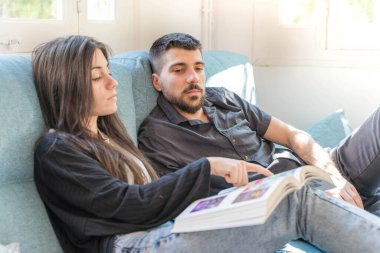 Coronavirus. Bir çift, Coronavirus sırasında evdeki karantinada kanepede oturuyor. Evdeki çift kanepede kitap izliyor ve konuşuyor. - Eve. Evde kal.. 