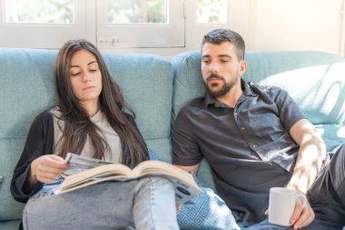 Coronavirus. Bir çift, Coronavirus sırasında evdeki karantinada kanepede oturuyor. Evdeki çift kanepede kitap izliyor ve konuşuyor. - Eve. Evde kal.. 