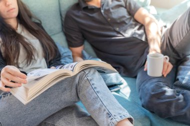 Coronavirus. Bir çift, Coronavirus sırasında evdeki karantinada kanepede oturuyor. Evdeki çift kanepede kitap izliyor ve konuşuyor. - Eve. Evde kal.. 