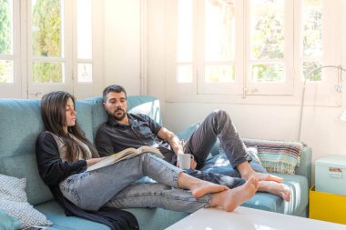 Coronavirus. Bir çift, Coronavirus sırasında evdeki karantinada kanepede oturuyor. Evdeki çift kanepede kitap izliyor ve konuşuyor. - Eve. Evde kal.. 