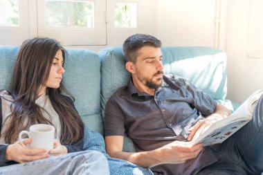 Coronavirus. Bir çift, Coronavirus sırasında evdeki karantinada kanepede oturuyor. Evdeki çift kanepede kitap izliyor ve konuşuyor. - Eve. Evde kal.. 