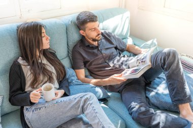 Coronavirus. Bir çift, Coronavirus sırasında evdeki karantinada kanepede oturuyor. Evdeki çift kanepede kitap izliyor ve konuşuyor. - Eve. Evde kal.. 