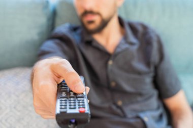 Coronavirus. Coronavirus sırasında evde karantinada kanepede oturup televizyon izleyen bir adam. Evdeki kanepede televizyon kumandalı bir adam. - Eve. Evde kal.. 