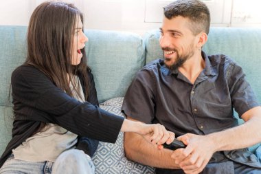 Coronavirus. Koronavirüs sırasında evde karantinada televizyon izleyen bir çift. Evdeki çift kanepede gülüyor ve televizyon kumandasını tartışıyor. - Eve. Evde kal.. 