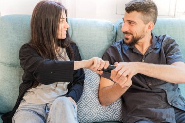 Coronavirus. Koronavirüs sırasında evde karantinada televizyon izleyen bir çift. Evdeki çift kanepede gülüyor ve televizyon kumandasını tartışıyor. - Eve. Evde kal.. 