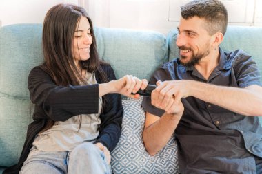 Coronavirus. Koronavirüs sırasında evde karantinada televizyon izleyen bir çift. Evdeki çift kanepede gülüyor ve televizyon kumandasını tartışıyor. - Eve. Evde kal.. 