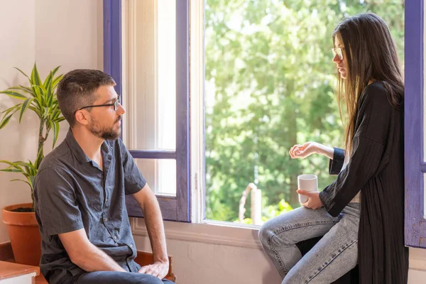 Coronavirus. Arkadaşları evde kahve yapıyor ve Coronavirus sırasında pencerenin yanında konuşuyorlar. Karantina konsepti. İşçiler. İzole edilmiş. Mola zamanı..