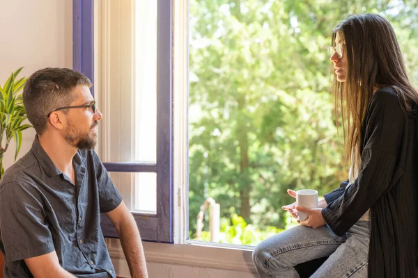 Coronavirus. Arkadaşları evde kahve yapıyor ve Coronavirus sırasında pencerenin yanında konuşuyorlar. Karantina konsepti. İşçiler. İzole edilmiş. Mola zamanı..
