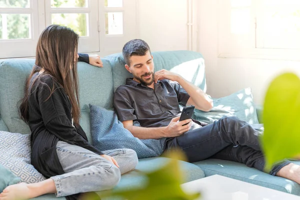 Coronavirus. Bir çift, Coronavirus sırasında evdeki karantinada kanepede oturuyor. Evdeki çift kanepede oturuyor, cep telefonuna bakıyor ve konuşuyor. - Eve. Evde kal.. 