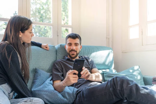 Coronavirus. A couple sitting on the couch on a quarantine at home, during  coronavirus. Couple at home on the couch and looking mobile phone and talking. Home. Stay home.