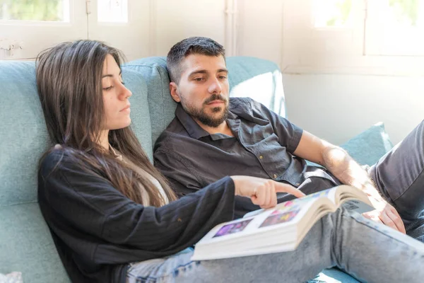 Coronavirus. Bir çift, Coronavirus sırasında evdeki karantinada kanepede oturuyor. Evdeki çift kanepede kitap izliyor ve konuşuyor. - Eve. Evde kal.. 