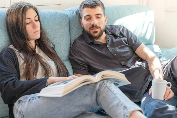 Coronavirus. A couple sitting on the couch on a quarantine at home, during  coronavirus. Couple at home on the couch and looking a book and talking. Home. Stay home.