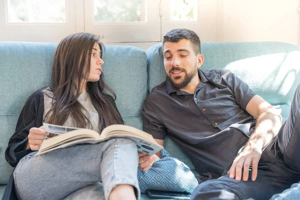 Coronavirus. Bir çift, Coronavirus sırasında evdeki karantinada kanepede oturuyor. Evdeki çift kanepede kitap izliyor ve konuşuyor. - Eve. Evde kal.. 