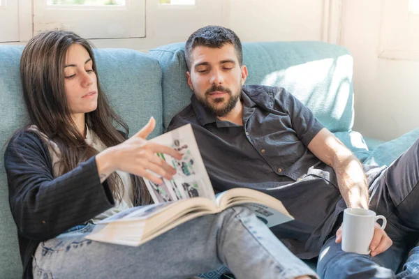 Coronavirus. A couple sitting on the couch on a quarantine at home, during  coronavirus. Couple at home on the couch and looking a book and talking. Home. Stay home.