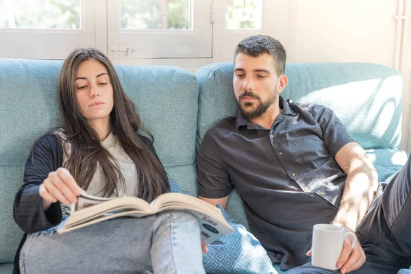 Coronavirus. Bir çift, Coronavirus sırasında evdeki karantinada kanepede oturuyor. Evdeki çift kanepede kitap izliyor ve konuşuyor. - Eve. Evde kal.. 