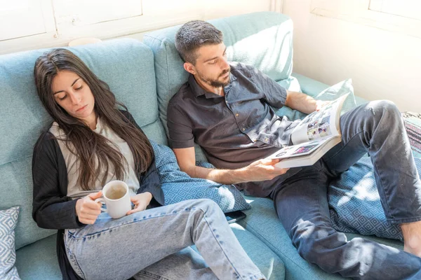 Coronavirus. A couple sitting on the couch on a quarantine at home, during  coronavirus. Couple at home on the couch and looking a book and talking. Home. Stay home.