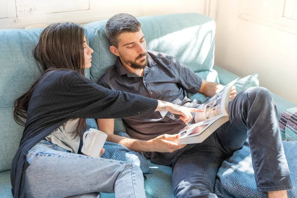 Coronavirus. Bir çift, Coronavirus sırasında evdeki karantinada kanepede oturuyor. Evdeki çift kanepede kitap izliyor ve konuşuyor. - Eve. Evde kal.. 