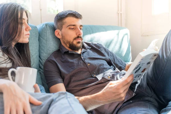 Coronavirus. Bir çift, Coronavirus sırasında evdeki karantinada kanepede oturuyor. Evdeki çift kanepede kitap izliyor ve konuşuyor. - Eve. Evde kal.. 