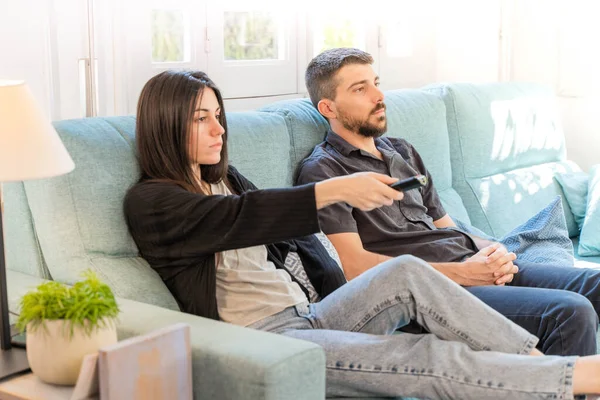Coronavirus. A couple sitting on the couch watching tv on a quarantine at home, during  coronavirus. Couple at home on the couch laughing and talking meanwhile watch tv. Home. Stay home.