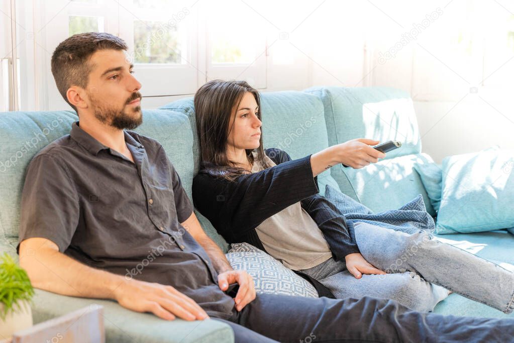 Coronavirus. A couple sitting on the couch watching tv on a quarantine at home, during  coronavirus. Couple at home on the couch laughing and talking meanwhile watch tv. Home. Stay home. 