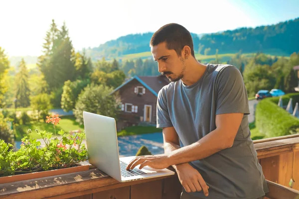 Young business man working with laptop on beautiful scenic mountain background. Business man working in a rural hotel. Freelancer. Traveler. Video call. Digital meeting.