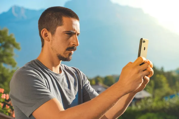 Young business man with mobile phone on beautiful scenic mountain background. Business man working in a rural hotel. Freelancer. Traveler. Taking pictures.