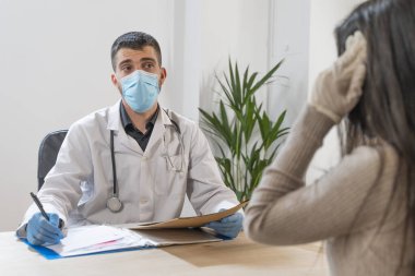 Coronavirus. Doktor sağlıksız kadını ziyaret ediyor. Doktor hastaya danışıyor. Önleme için yüz maskesi ve lastik eldiven kullanıyorlar. Hasta bakımı. Teşhisler. Coronavirus belirtileri