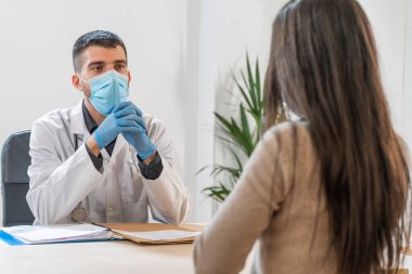 Coronavirus. Doktor sağlıksız kadını ziyaret ediyor. Doktor hastaya danışıyor. Önleme için yüz maskesi ve lastik eldiven kullanıyorlar. Hasta bakımı. Teşhisler. Coronavirus belirtileri