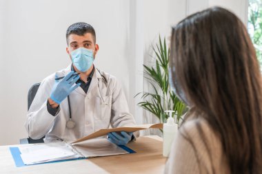 Coronavirus. Doktor sağlıksız kadını ziyaret ediyor. Doktor hastaya danışıyor. Önleme için yüz maskesi ve lastik eldiven kullanıyorlar. Hasta bakımı. Teşhisler. Coronavirus belirtileri