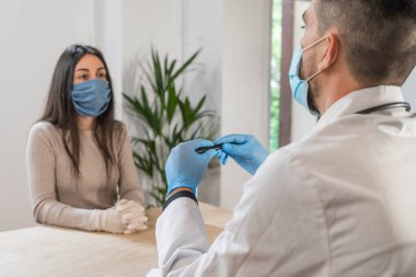 Coronavirus. Doktor sağlıksız kadını ziyaret ediyor. Doktor hastaya danışıyor. Önleme için yüz maskesi ve lastik eldiven kullanıyorlar. Hasta bakımı. Teşhisler. Coronavirus belirtileri. Temizleyici jel..
