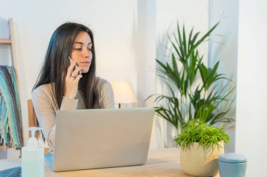 Evde bilgisayarla çalışan bir iş kadını. Küçük bir şirket çalışıyor ve iş yapıyor. Karantina sırasında evde çalışmak. Küçük ofis. Coronavirus. Temizleyici jel..
