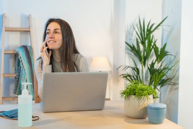 Evde bilgisayarla çalışan bir iş kadını. Küçük bir şirket çalışıyor ve iş yapıyor. Karantina sırasında evde çalışmak. Küçük ofis. Coronavirus. Temizleyici jel..
