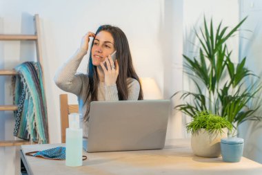 Evde bilgisayarla çalışan bir iş kadını. Küçük bir şirket çalışıyor ve iş yapıyor. Karantina sırasında evde çalışmak. Küçük ofis. Coronavirus. Temizleyici jel..