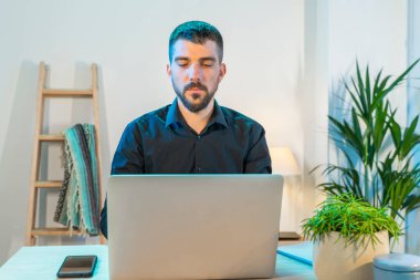 Evde bilgisayarla çalışan bir iş adamı. Küçük bir şirket çalışıyor ve iş yapıyor. Karantina sırasında evde çalışmak. Küçük ofis. Coronavirus. Temizleyici jel ve yüz maskesi..