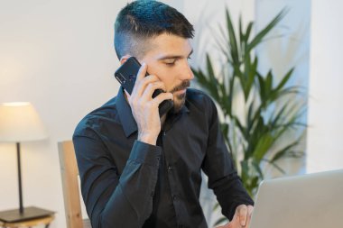 Evde bilgisayar ve cep telefonuyla çalışan bir iş adamı. Küçük bir şirket çalışıyor ve iş yapıyor. Karantina sırasında evde çalışmak. Küçük ofis. Coronavirus. Temizleyici jel..