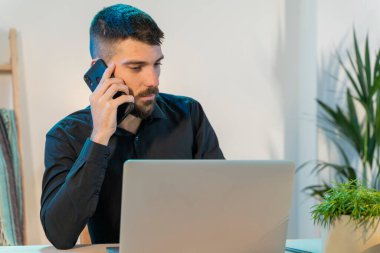 Evde bilgisayar ve cep telefonuyla çalışan bir iş adamı. Küçük bir şirket çalışıyor ve iş yapıyor. Karantina sırasında evde çalışmak. Küçük ofis. Coronavirus. Temizleyici jel..